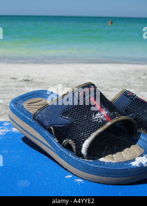ein paar Sandalen links am Strand, während Besitzer im Meer im Hintergrund Schwimmen ist Stockfoto