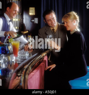 GUT GEKLEIDETE PAAR TRINKEN CHAMPAGNER IN EINE COCKTAIL-LOUNGE AM ABEND Stockfoto