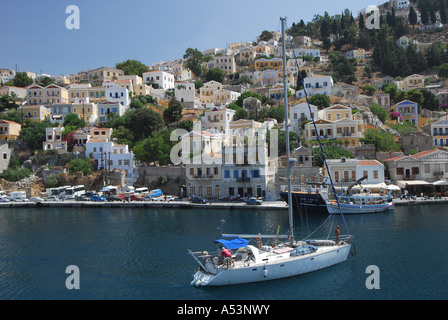 Eine Yacht in Yialos Hafen in Sými Stadt auf der griechischen Insel Sými mit Neo-klassizistischen Häuser auf den steilen Hang hinter Stockfoto