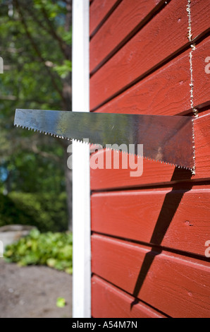 Sägen durch ein rotes Brett an der Wand mit handsäge Stockfoto