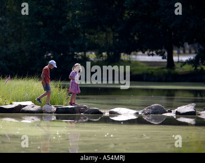 Zwei kleine Kinder, die über einen Gartenteich mit Sprungbrett, Finnland Stockfoto