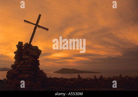 Überqueren Sie auf Steinkairn auf dem Gipfel der Taquile Insel bei Sonnenuntergang, Amantani Insel in der Ferne, Titicaca See, Peru Stockfoto