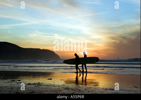 Zwei männliche Surfer Silhouette gegen den Sonnenuntergang Himmel am Strand von Perranporth an der Nordküste Cornish. Stockfoto