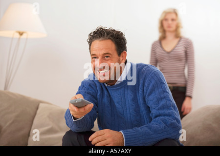 Mann sitzt auf dem Sofa, Holding-Fernbedienung, Tochter im Hintergrund Stockfoto