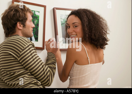 Junges Paar Aufhängen von Bilderrahmen, lächelnde Frau Stockfoto