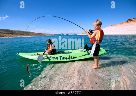 Junge stand auf Felsen Fang einen Fisch als seine Schwester Uhren aus grünem Kunststoff-Kajak am Lake Powell Arizona-Utah Stockfoto