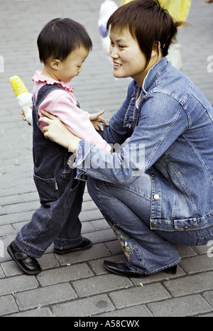 CHINA SHANGHAI modernen jungen chinesischen Mutter in Jeans gekleidet hilft Tochter Kleinkind einen Snack von geröstetem Mais zu essen Stockfoto