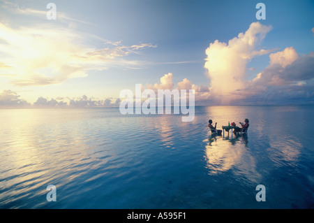 Paar sitzt am Tisch teilen Sonnenuntergang trinken in Lagune inmitten des Pazifischen Ozeans. Ruhe und Einsamkeit im Urlaubsparadies Stockfoto