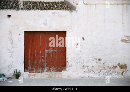 Alte Holztür der zerfallenden Gebäude. Müll verstreut auf Asphalt. Pathetisch Pflanze wächst aus Riss in der Wand. Stockfoto