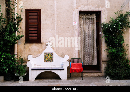 Ein Blick auf eine Bank und Stuhl außerhalb der Vorderseite eines Hauses.  Gardine in Tür. Hölzerne Auslöser. Kletterpflanze an der Wand Stockfoto