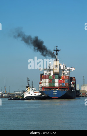 Ankommender Frachtcontainer Frachtschiff & schwarzer Rauch gestapelt mit Ladung Transportcontainer Schlepper schiebt in Richtung Kräne Felixstowe Port Suffolk UK Stockfoto