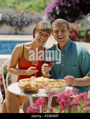 junges Paar Essen und trinken Wein auf der Terrasse am Swimmingpool Stockfoto