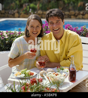 junges Paar Essen und trinken Wein auf der Terrasse am Swimmingpool Stockfoto