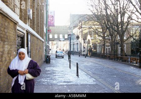 Eine Frau kommt auf dem Bürgersteig in der Brick Lane in London Stockfoto