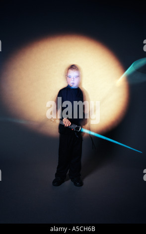 Eine vertikale Farbbild eines kleinen Jungen in einem dunklen Kostüm mit weißen Gesicht malen ein blaues Licht Schwert schwingen Stockfoto