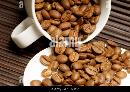 Nahaufnahme von Kaffeebohnen in der Tasse, die auf die Untertasse verschüttet werden Stockfoto