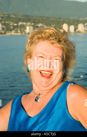 Mitte 50 Jahre lächelnde Frau mit blauen Oberteil und Halskette auf Kreuzfahrtschiff Auslaufen aus dem Hafen von Vancouver BC Kanada Stockfoto