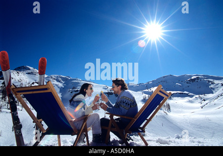 Paar sitzt auf Liegestuhl im Schnee Toasten Gläser, Seitenansicht Stockfoto