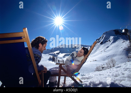 Junges Paar sitzt auf Liegestühlen im Alpen, Lächeln Stockfoto