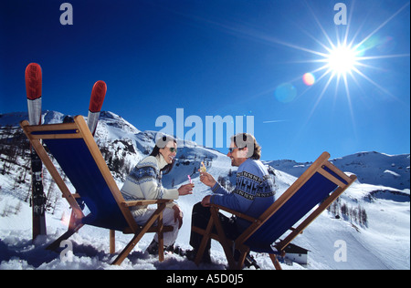 Paar sitzt auf Liegestuhl im Schnee Toasten Gläser, Seitenansicht Stockfoto