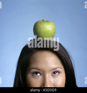 Junge Frau balancieren Apfel auf Kopf, Blick nach oben, Nahaufnahme Stockfoto