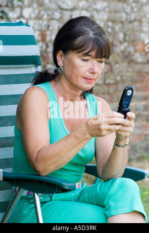 Woman applying im Garten sitzen auf Stuhl SMS auf Handy Stockfoto