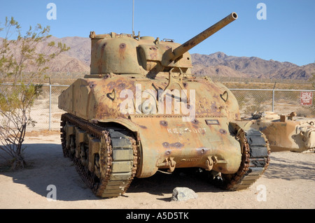 Ein verrosteter Sherman M4-Tank steht in einem Wüstenschauplatz im General Patton Museum in Kalifornien, mit zerklüfteten Bergen im Hintergrund. Stockfoto
