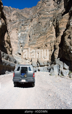 Ein silberner SUV fährt auf einer Schotterstraße durch die schmalen, hoch aufragenden Felswände des Titus Canyon im Death Valley National Park, Kalifornien. Stockfoto