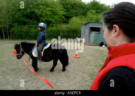 schwarze Mädchen mit Shetland-Ponys, die mit ihrer Mutter in einem Feld fahren zu lernen Stockfoto