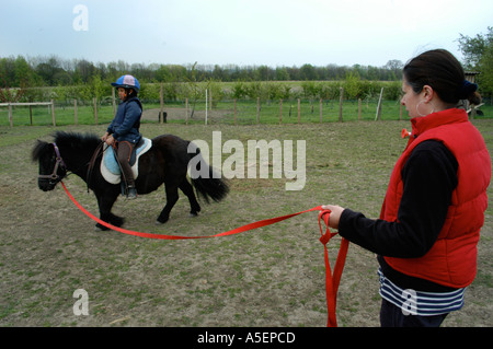 schwarze Mädchen mit Shetland-Ponys, die mit ihrer Mutter in einem Feld fahren zu lernen Stockfoto