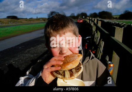 Ein kleiner Junge essen Burger. Beißen in einen großen Burger illustrieren Fettleibigkeit durch Junk-Food Essen. Stockfoto