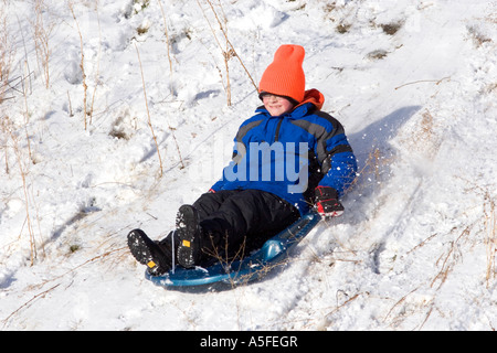 Junge einen Schnee bedeckten Hügel in Idaho hinunter rodeln Stockfoto