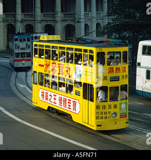 Typische helle gelbe lokale elektrische Straßenbahn mit roten chinesischen Schrift auf allen Seiten und voller Passagiere Hong Kong Stockfoto