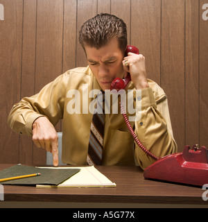 Caucasion Mitte Erwachsenen Retro-Geschäftsmann am Schreibtisch Gespräch am Telefon mit wütenden Ausdruck Stockfoto