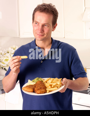 MANN IN DER KÜCHE ESSEN FISCH UND CHIPS Stockfoto