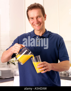 MANN IN DER KÜCHE GIEßEN ORANGE JUICE Stockfoto