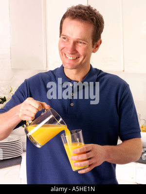 MANN IN DER KÜCHE GIEßEN ORANGE JUICE Stockfoto