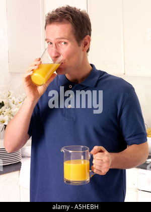 MANN IN DER KÜCHE TRINKEN ORANGE JUICE Stockfoto