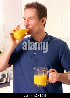 MANN IN DER KÜCHE TRINKEN ORANGE JUICE Stockfoto