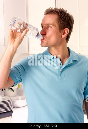 MANN IN DER KÜCHE AUS FLASCHE WASSER TRINKEN Stockfoto