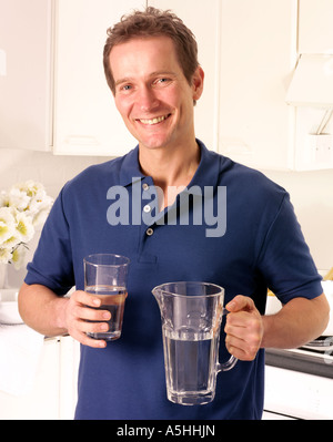 MANN IN DER KÜCHE HALTEN GLAS WASSER Stockfoto