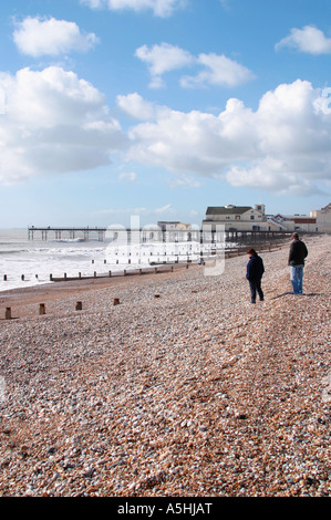 Mann und Frau, die bei Flut im Winter in der Nähe des Bognor Regis Pier auf Schindeln gehen Stockfoto