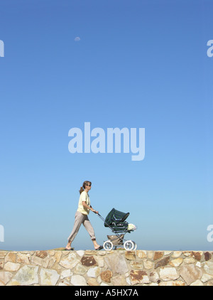 Junge Frau schieben Kinderwagen zu Fuß auf Steinmauer Stockfoto