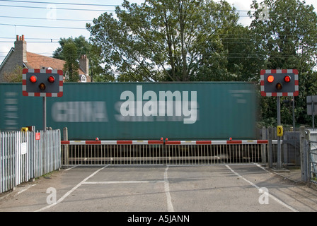 Eisenbahn Schienen rot blinkende Warnleuchte Zeichen Bahnübergang Barriere Tore Land Straße Container Zug Bewegungsunschärfe Margaretting Essex England UK Stockfoto