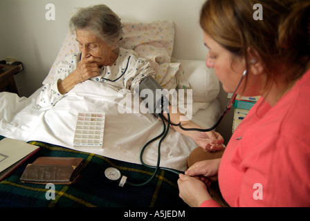 Eine ältere Frau sitzt in ihrem Bett mit ihren Blutdruck durch eine Krankenschwester, die ihr Zuhause zu besuchen. Stockfoto