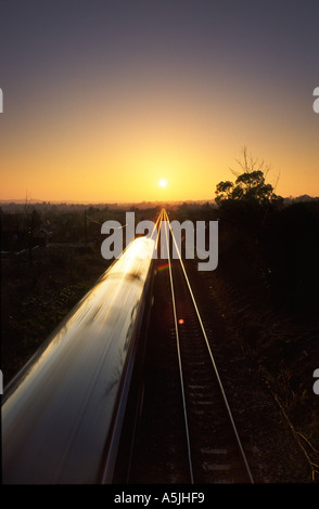 Trainieren Sie, fahren Sie direkt in Richtung der untergehenden Sonne am fernen Horizont in Bradford Abbas Dorf Dorset county England UK Stockfoto