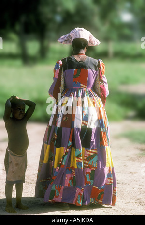 Herero-Frau trägt einen traditionellen Patchwork-Kleid und Kopfschmuck mit einem Kind-Botswana Stockfoto