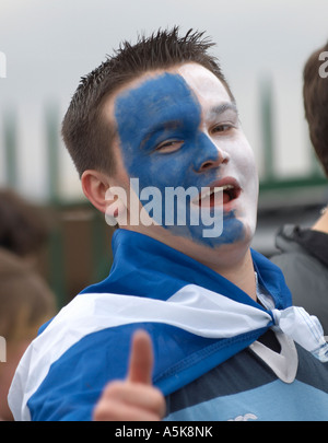 Junger Mann mit Gesicht gemalt in schottische Flagge Farben tragen eine schottische Flagge Stockfoto