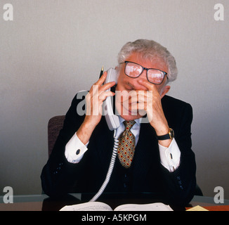 Älterer Mann am Telefon in seinem Büro sitzt an seinem Schreibtisch betroffenen müde und überarbeitet Stockfoto