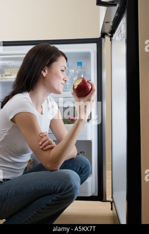 Frau zu essen Apfel vor offenen Kühlschrank Stockfoto